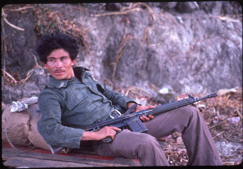 Armed guerrilla sits against a rock in the countryside, La Palma, 1983