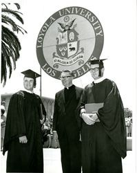 Students and Jesuit at Loyola University commencement in front of university banner, 1972