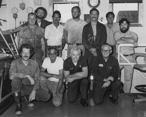 Shipboard marine crew, including Joseph Clarke (second from left, kneeling) the captain of the D/V Glomar Challenger (ship), during Leg 96 of the Deep Sea Drilling Project. 1979