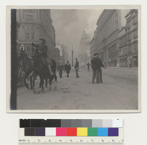 Market St. (800 block). [Soldiers and police officers in street before Flood Building at Powell and Eddy. Call Building burning in distance, center; Emporium department store, right.]