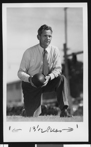 University of Southern California head football coach Jess Hill, on one knee, holding football, in tie and tweed pants, Bovard Field, 1951
