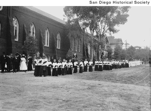 Procession of choirboys led by a priest outside a church for the groundbreaking of the 1915 Exposition