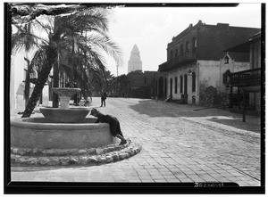 Child leaning against the fountain at Olvera Street with the City Hall in the background, ca. 1930