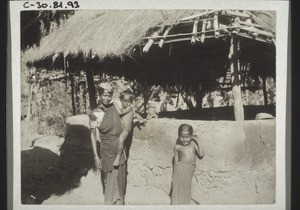 Frau mit 2 Kindern vor einer Hütte
