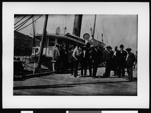 Group of Sunset Club members posing on the dock in front of the boat The Warrior, ca.1910