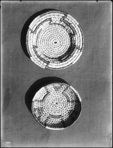 Two Indian baskets displayed against a cloth backdrop, ca.1900