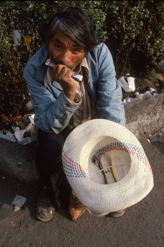 A man plays harmonica on street, Mexico, ca. 1983