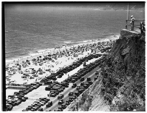 View of a crowded beach near Pacific Coast Highway with a cliff in the foreground