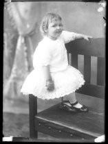 Portrait of toddler in lace dress, perched on chair