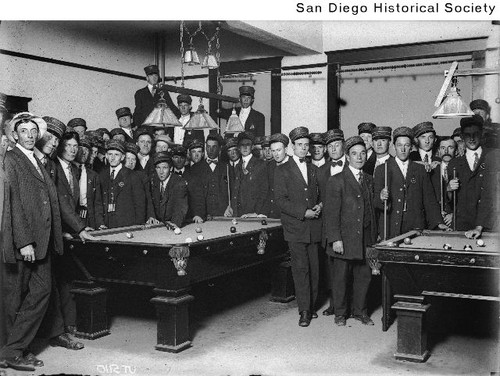 A large group of men standing around two pool tables