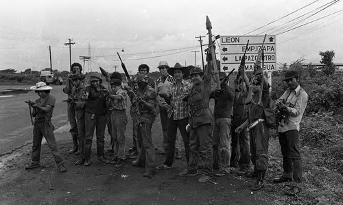 A group of Sandinistas hold their firearms while standing in front of a street sign, Nicaragua, 1979