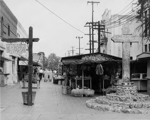 Shot of Olvera Street looking north. Cross and puestos and people on west side of street