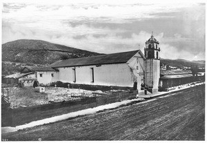 Exterior view of Mission San Buenaventura, showing the east door and tower of the church, ca.1875