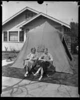 Two teenage girls seated outside of a tent in front of a house after the Long Beach earthquake, Southern California, 1933