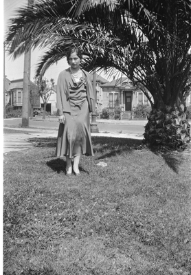 Young woman standing in front yard next to palm tree