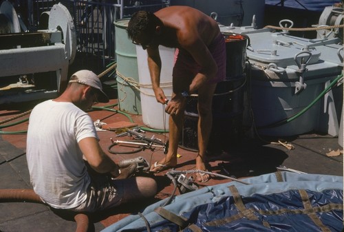 Scientific members of the Swan Song Expedition (1961) are shown here making repairs to the \"sampler\" water collection bag. This expedition explored the North Pacific at the equator and Eastern Tropical Pacific on the research ship Argo. The expedition collected large water samples for analysis, studied the Cromwell Current (Pacific Equatorial Undercurrent), and undertook a limited biological program for the Inter-American Tropical Tuna Commission. September 1961