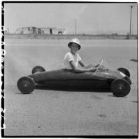 Al Pedrosa sitting in his soap box derby car on a barren stretch of road, Los Angeles, 1946