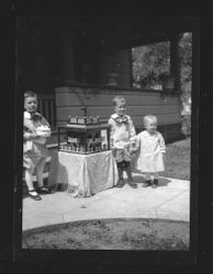 Children's birthday party with three young toddlers around a table with a fort-like toy, about 1920-30