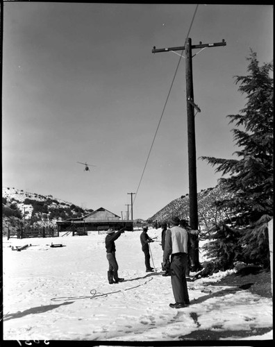 Linemen working working on pole line in the snow with helicopter flying near by