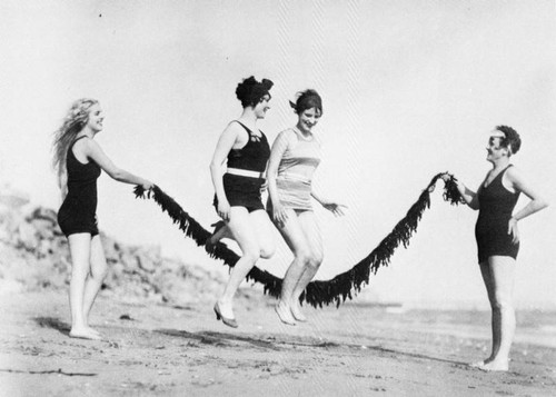 Women playing jump rope at the beach, a postcard