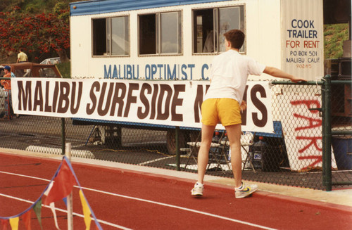 A man stretching next to the "Malibu Surfside News" banner