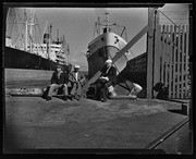 Three men sitting on waterfront dock, California Labor School