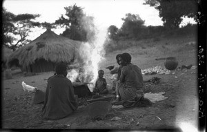Women and children sitting by a fire, between Guijá and Pafuri, Mozambique, ca. 1940-1950