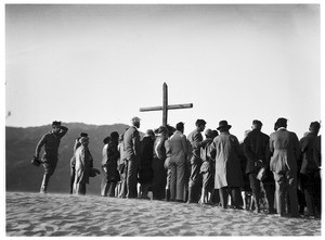 Group of people congregated around a cross for a funeral in the desert