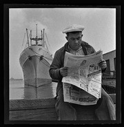 Man reading newspaper on waterfront dock, California Labor School