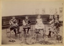 Group of four children on tricycles, with dolls