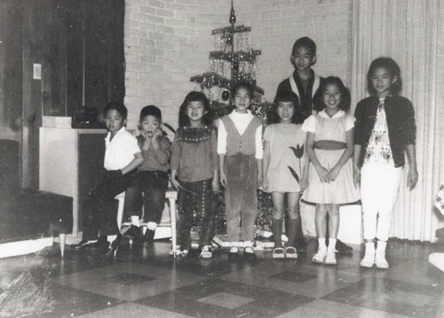 Children posed in front of a small Christmas tree with tinsel