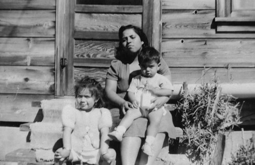 Adelia Lopez and children in front of home, [graphic]