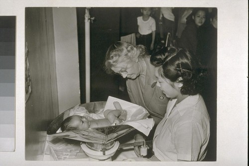 [Nurse and woman weighing infant.]