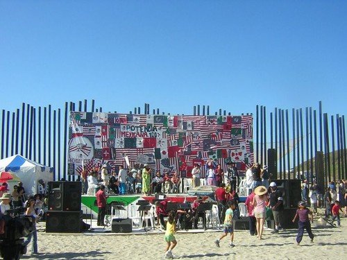 One Flew Over the Void (Bala perdida): border fence decorated with banners behind performance stage