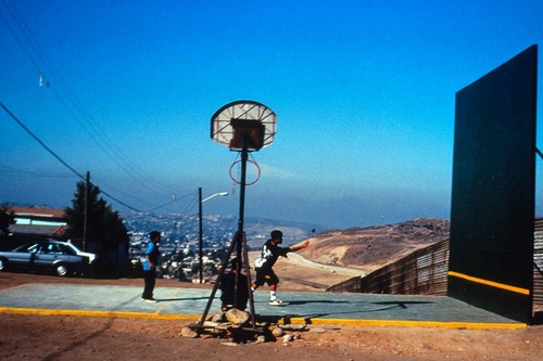 The Rules of the Game: ball court and border fence with children playing