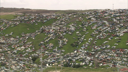 Osmosis and Excess: film still depicting Tijuana hillside covered in junk cars