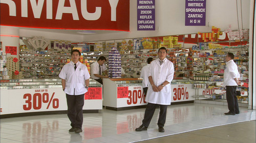 Osmosis and Excess: film still depicting the interior of a drug store with pharmacists