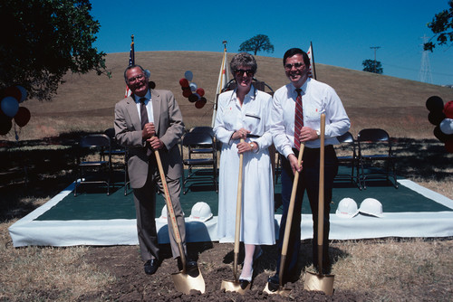 Three unknown persons posing for the ceremonial groundbreaking with shovels