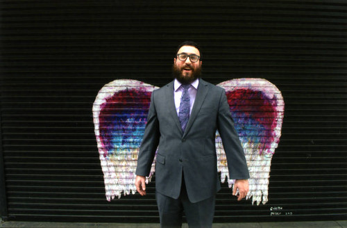 Unidentified man in a grey suit posing in front of a mural depicting angel wings