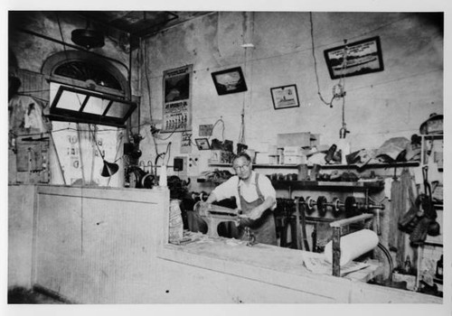 Masao Taketa working behind counter in shoe repair shop [?]