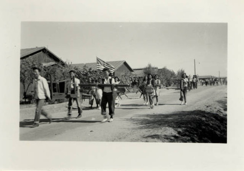 Students of Poston II Relocation Center school moving out of barrack building, waving American flag