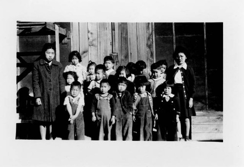 Group portrait of pre-school or elementary students in front of barrack classroom at Poston II Relocation Center