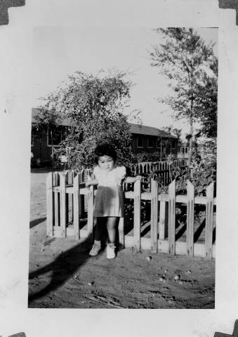 Gloria Sato standing alongside picket fence at Granada Relocation Center