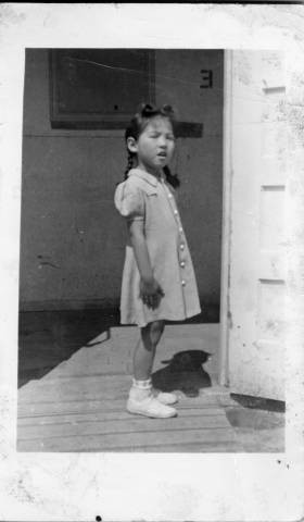 Geraldine Setsuko Nakano standing outside doorway to barracks at Granada Relocation Center