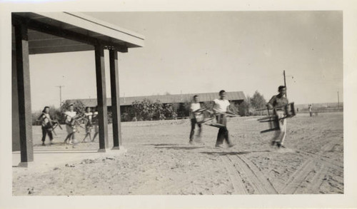 Students with furniture from Poston II Relocation Center school rounding corner of new school building