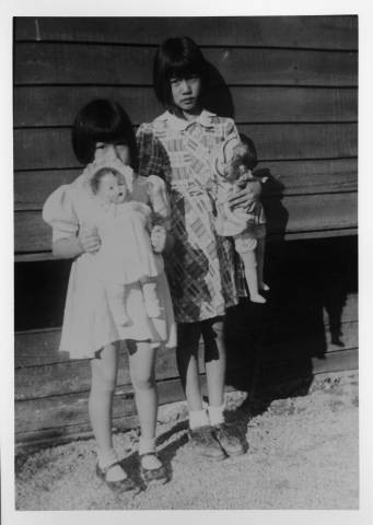 Reiko Nagumo and Mariko Nagumo holding dolls outside building