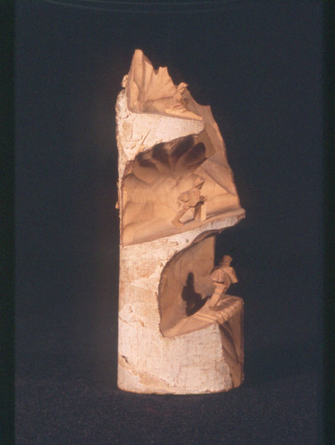 Wood carving of two figures climbing a mountain and one sitting at top