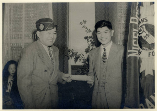 Two Japanese American men next to Sacramento Nisei VFW Post No. 8985 flag