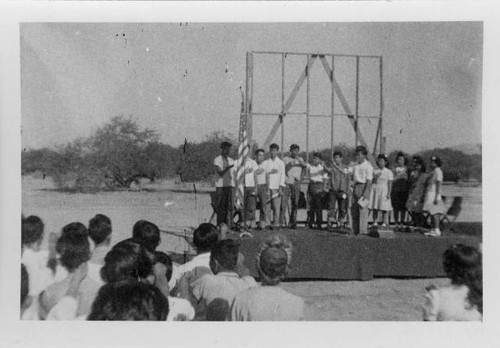 Students reciting the American Pledge of Allegience on stage during ceremony at Poston II school