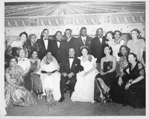 Group photograph at Slim Jenkins Bar and Restaurant (left to right): Hazel Vaughns (4th woman seated), George Vaughns (standing), Byron Rumford, Aramis Fouche, Ted Hardiman, Kate [illegible]